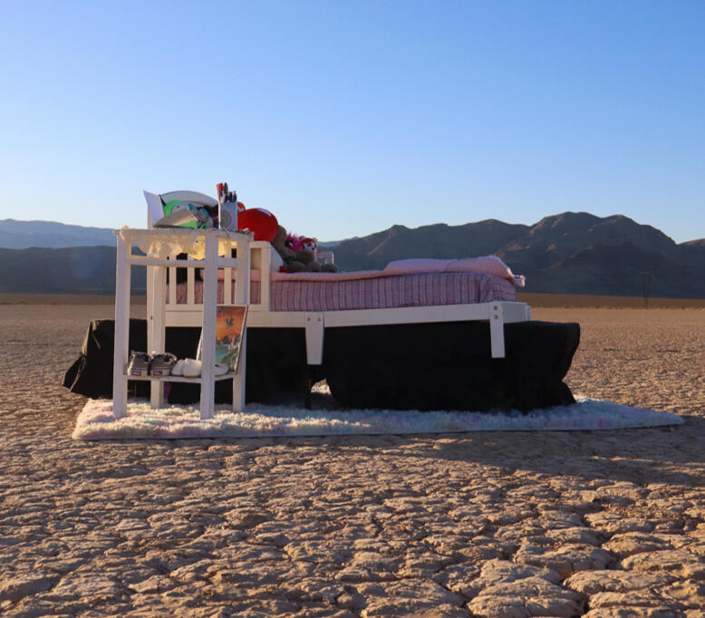Image of sculpture by Haide Callejas. Features Otomi artisan embroidery on a suspended reclaimed fabric banner. The fabric is dyed pink and green and assembled in a garden-scape visage. Piece is supended from a clothesline.