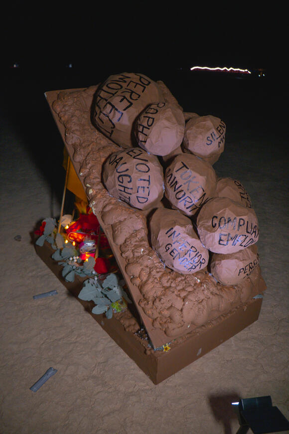Image of sculpture by Abney Wallace. Features vertical pieces of dimensional lumber painted various shades of white and blue arranged in a crop circle with circular lines scratched into lake-bed.