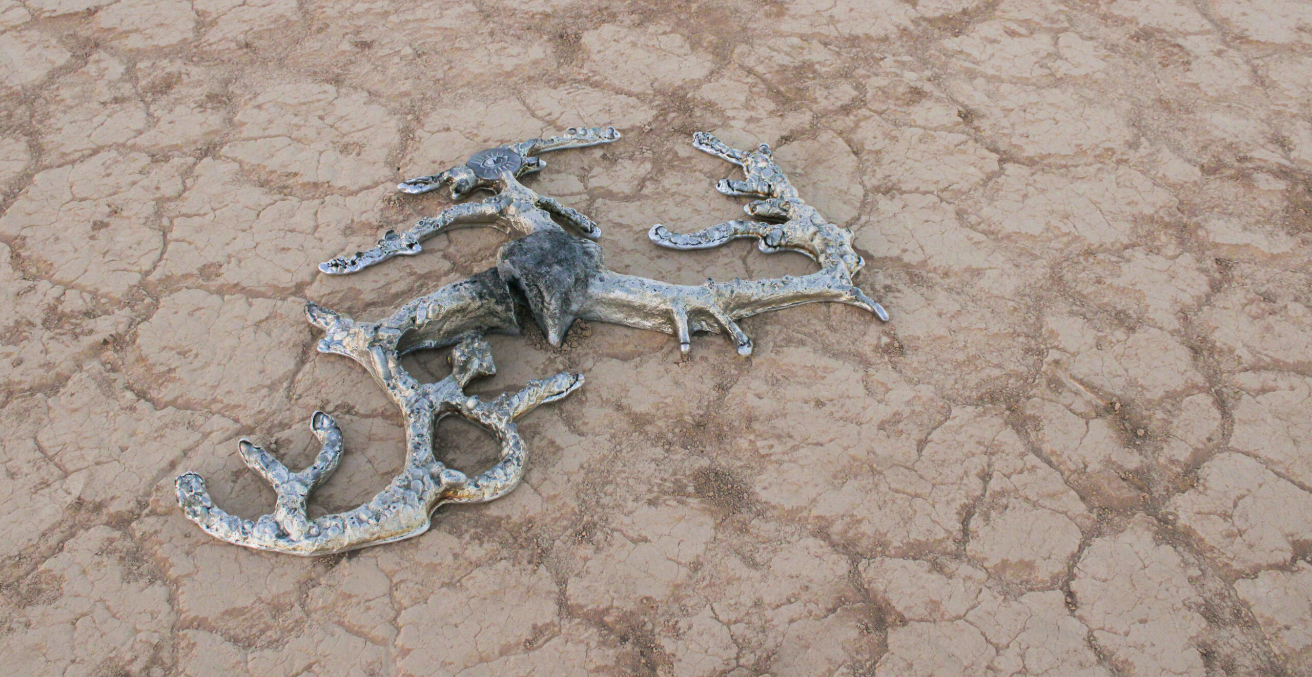 Image of sculpture by experimental foundry group Aluminati. Features cast aluminum object with three tendrils stemming from a core, created during a public event where visitors made their physical mark into a sand mold to create the impressions on surface.