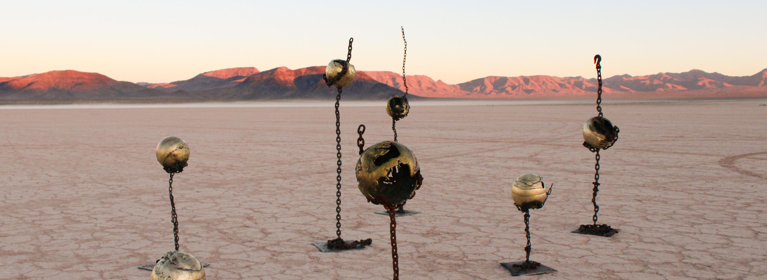 Image of sculpture by Bailey Anderson and Iulia Filipov-Serediuc. Features seven unique cast brass spheres suspended vertically in welded steel chain, of various heights.