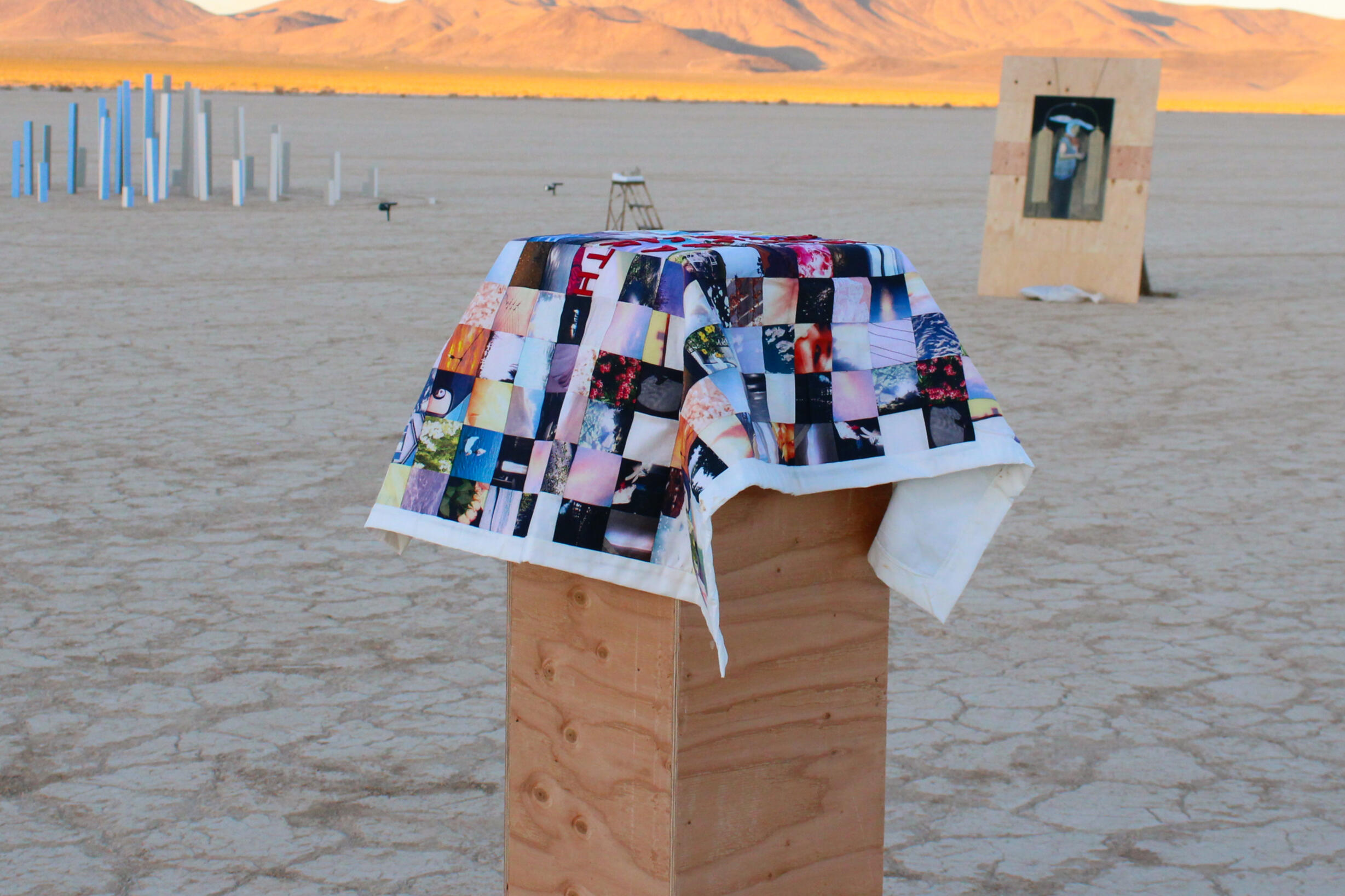 Image of sculpture by Clara Tang. Features quilt composed of individually sewed on fabric photo prints. Quilt is draped over wooden pedestal.