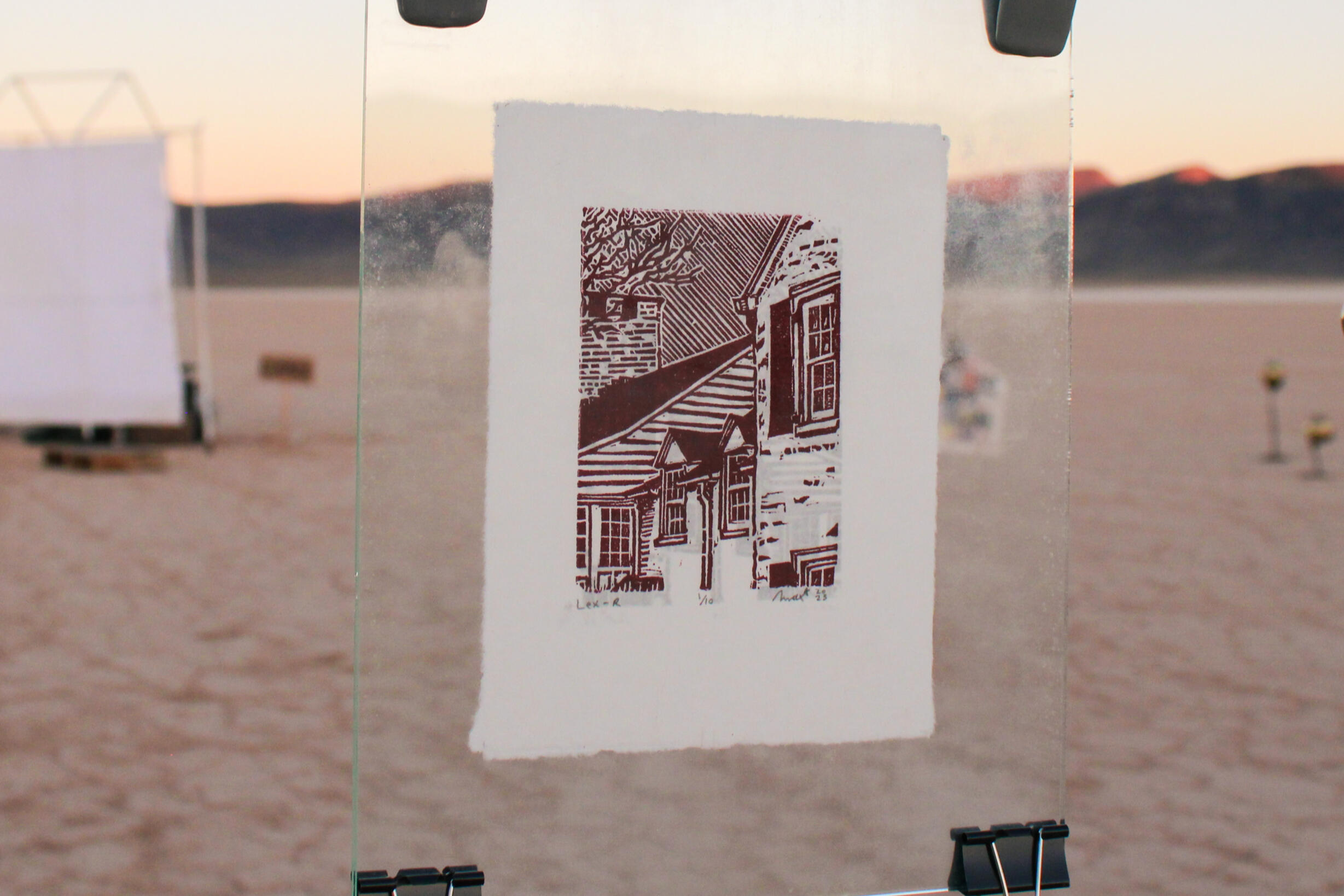 Image of print by Max Krosta. Features house in perspective view. Print is suspended in glass and hung from clothesline.